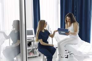Clínicas de estética - mujer sentada en una camilla sujetando una carpeta con documentación en la clínica de estética mientras habla con el especialista