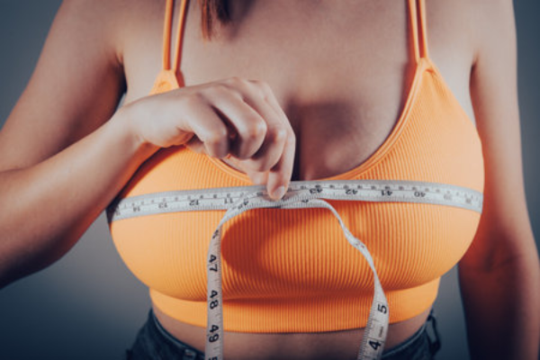Las mejores clínicas de reducción de pecho en Palma de Mallorca - Mujer con top naranja usa una cinta métrica para medir el tamaño de sus senos previo a una cirugía
