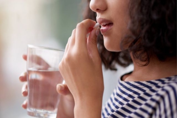 clínicas de levantamiento de pecho en Bilbao - mujer joven tomando una pastilla con un vaso con agua en la mano