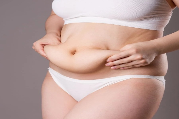 Mujer con sobrepeso en ropa interior blanca sujeta con sus manos el exceso de grasa que le sobra en el abdomen