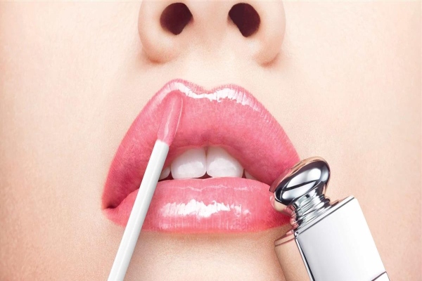 Joven de tez blanca aplica un gloss para mejorar la apariencia y el volumen de sus labios
