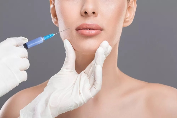 Cirujano sostiene la barbilla de una paciente para infiltrar una solución reabsorbible y completamente natural en sus labios