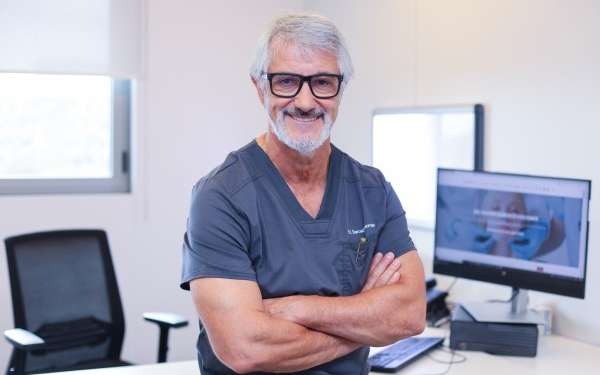 Doctor en rinoplastia en Barcelona - Perfil del Dr. Barceló Colomer con lentes y ropa de trabajo desde su consultorio