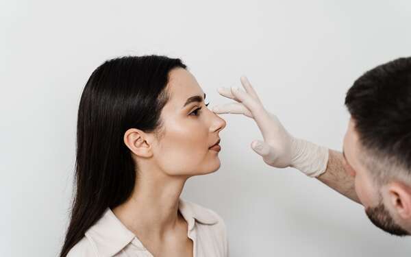 Clínicas de rinoplastia en Málaga - Médico especialista evalúa con su mano la nariz perfilada de una mujer joven