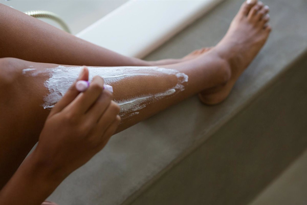 Mujer de piel morena se depila las piernas con máquina tras salir de la ducha