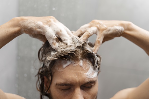 Hombre lavando su cabello con champú mientras realiza un masaje con la yema de sus dedos, para estimular la producción de sebo