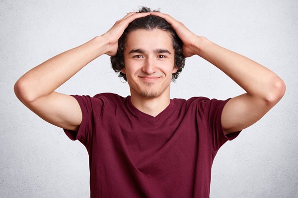 Cuántos pelos tenemos en la cabeza - Hombre sonriendo con las manos en la cabeza, sosteniendo su cabello largo y rizado