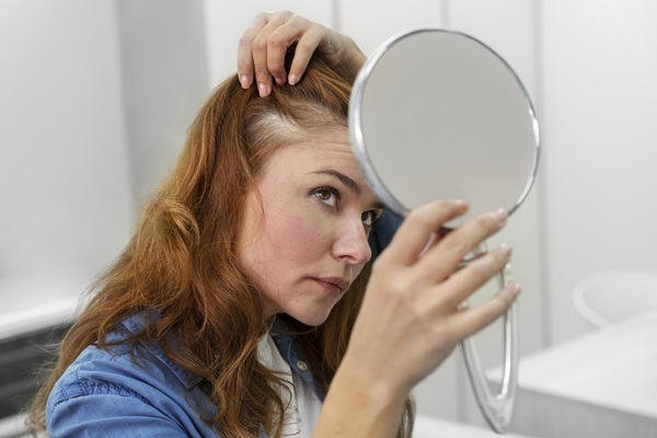 Cuántos pelos tenemos en la cabeza - Mujer observando en el espejo que la caída de cabello es cada vez mayor, debido a los cambios hormonales