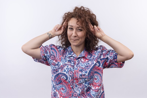 Cuántos pelos tenemos en la cabeza - Mujer posando con su manos apuntando hacia el cabello, el cual lo tiene rizado y de color castaño