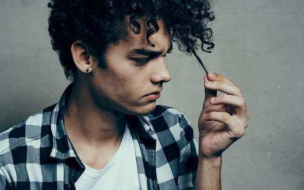 Calvicie y pelo graso - Joven de cabello rizado se detiene a observar un mechón de pelo sin brillo y con aspecto pastoso