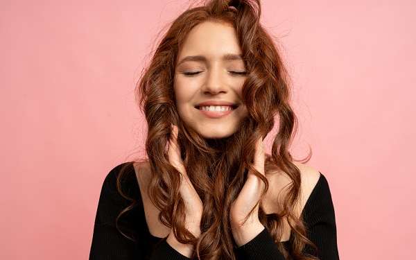 Cómo cuidar el pelo en las mujeres -mujer sonriente acariciando su cabello tras una rutina de cómo cuidar el pelo