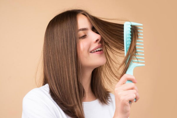 Kit para el cuidado del cabello - Joven sonriente peina su cabello sano y trabaja en su cuidado capilar