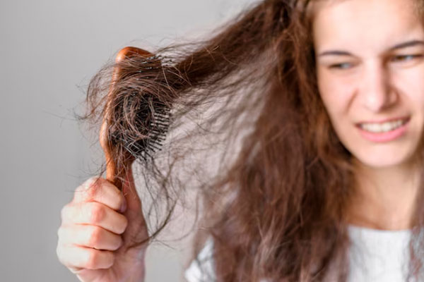 Kit para el cuidado del cabello - Joven lucha con el cepillo en un intento por desenredar su cabello seco