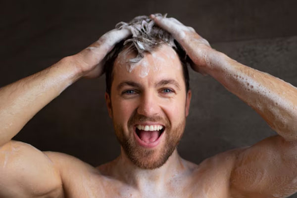 Kit para el cuidado del cabello - Hombre sonriente con espuma en la cabeza lava su cabello con champú