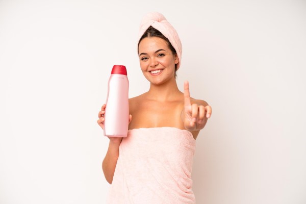 cuidar el pelo en los hombres - mujer después de la ducha con un bote de champú en la mano y la otra marcando el numero 1