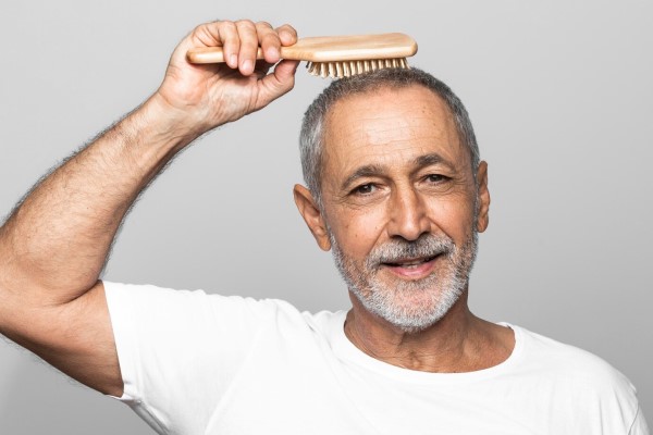 hombre mayor cepillándose su melena con canas por el envejecimiento del cabello