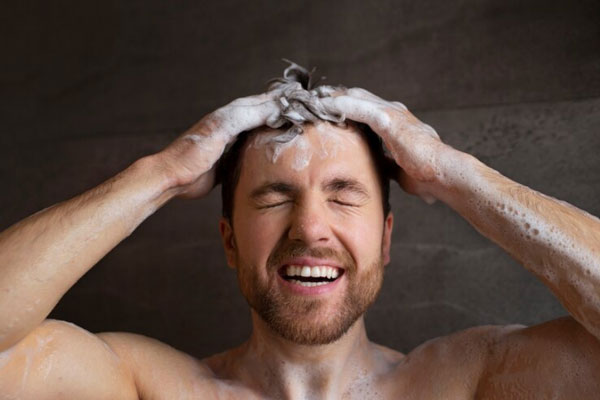 Hombre con champú y manos en la cabeza cierra los ojos mientras lava su cabello