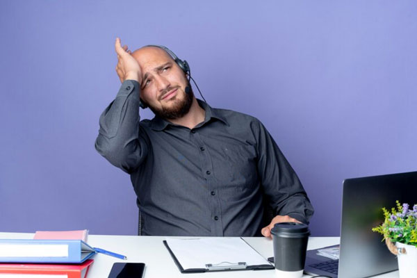 Salud mental en el hombre - Hombre calvo, estresado y con auriculares atiende llamadas desde su escritorio