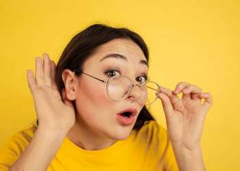tipos de orejas - Joven con gafas afina el oído para escuchar con atención