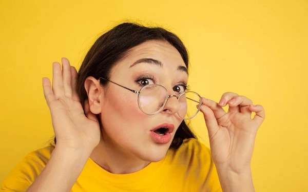 tipos de orejas - Joven con gafas afina el oído para escuchar con atención